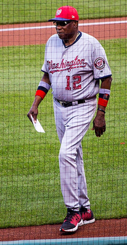 A man wearing a baseball uniform walks across a baseball field.