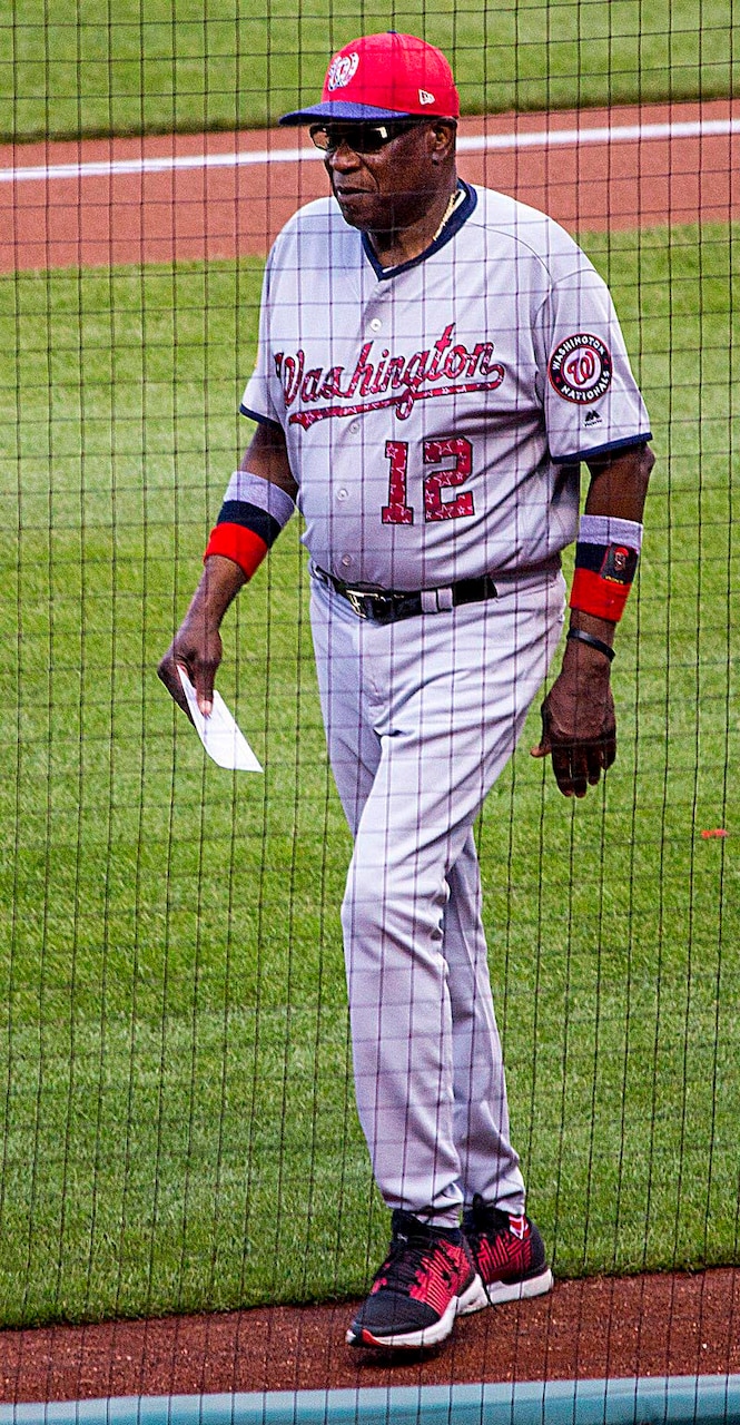 A man wearing a baseball uniform walks across a baseball field.