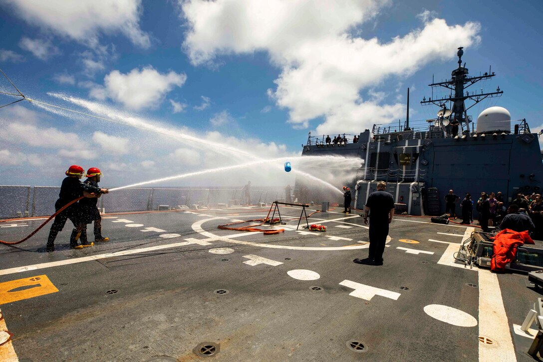 Sailors compete in a fire hose tug-of-war aboard a ship at sea.