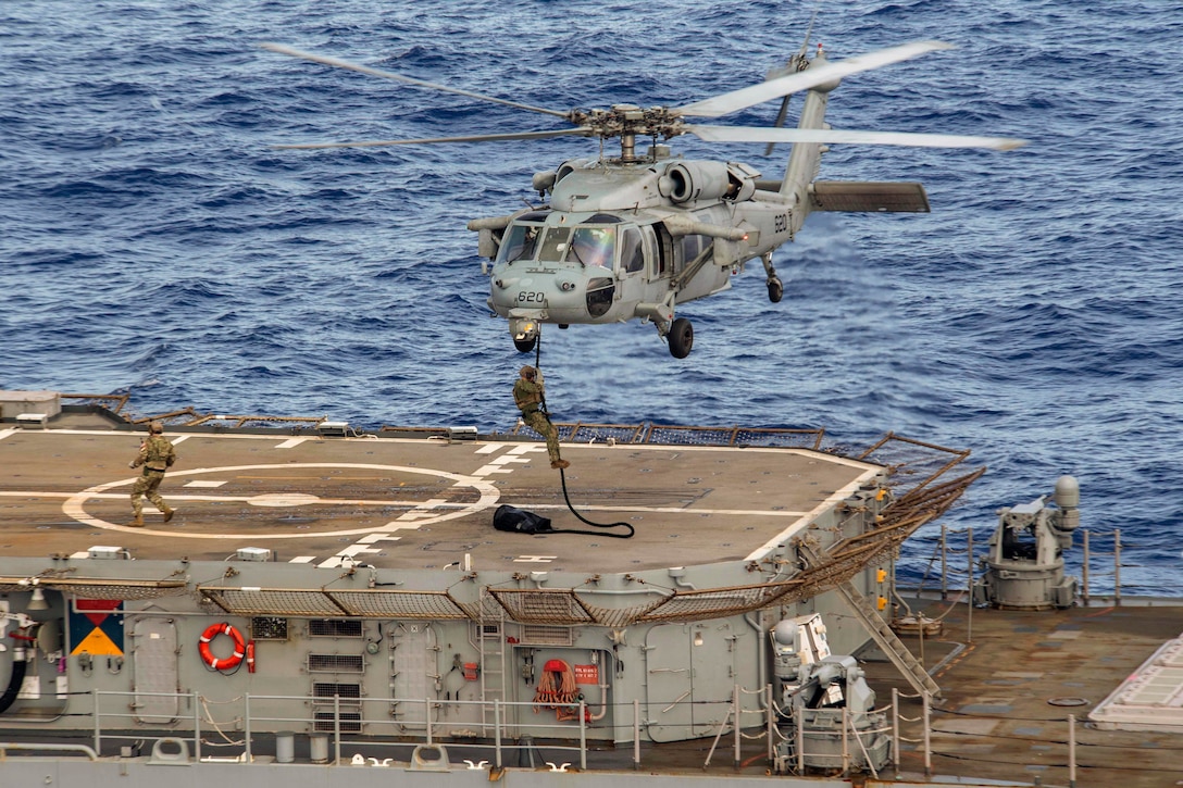 A sailor rappels from a helicopter onto a ship at sea.