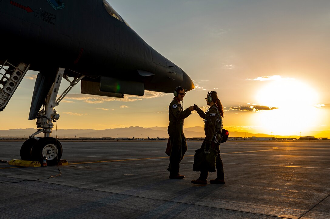 Two airmen, shown in silhouette, bump fists by an aircraft on a flightline.