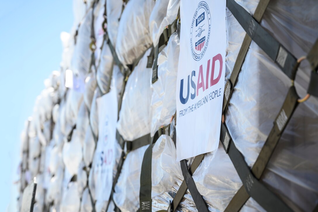 Web mesh is wrapped around cargo. A paper sign reads "USAID."