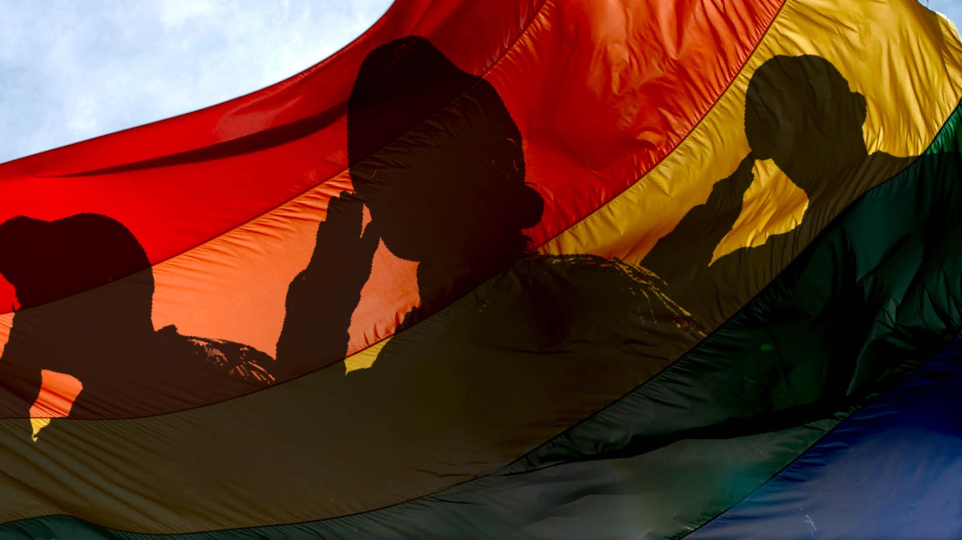 A graphic with servicemember silhouettes saluting over an LGBTQ+ flag.