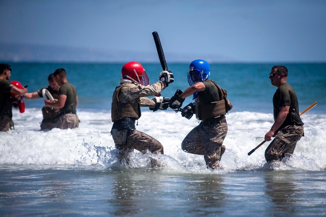 Two Marines use pugil sticks against each other while standing in water.