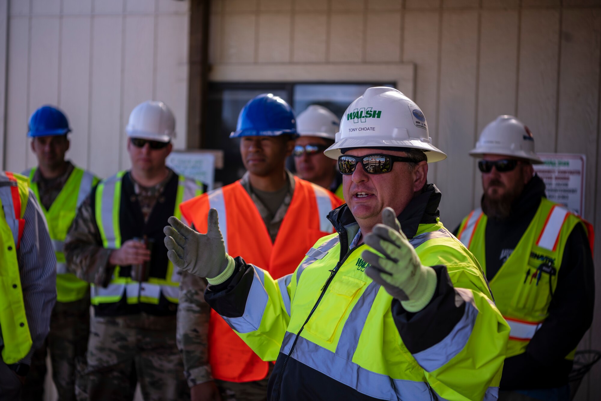 A man in construction clothing talks to a group of people.