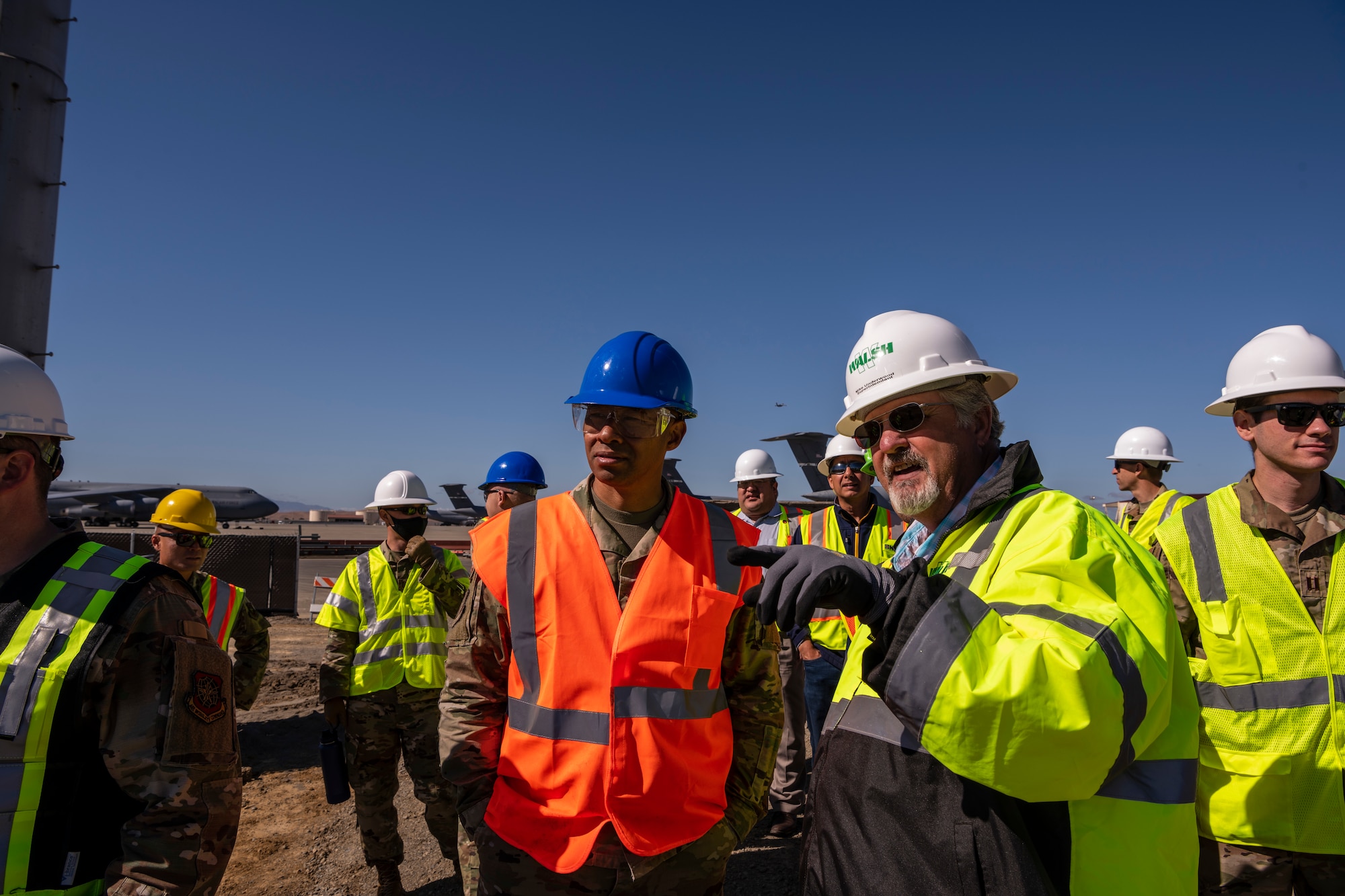 A man is bright construction clothes talks to another man wearing a military uniform while also wearing bright colors over his uniform.