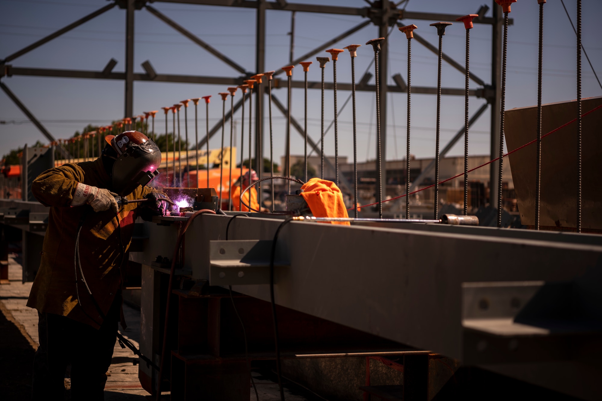 A man is wearing a helmet while he is welding a long beam on a construction site.