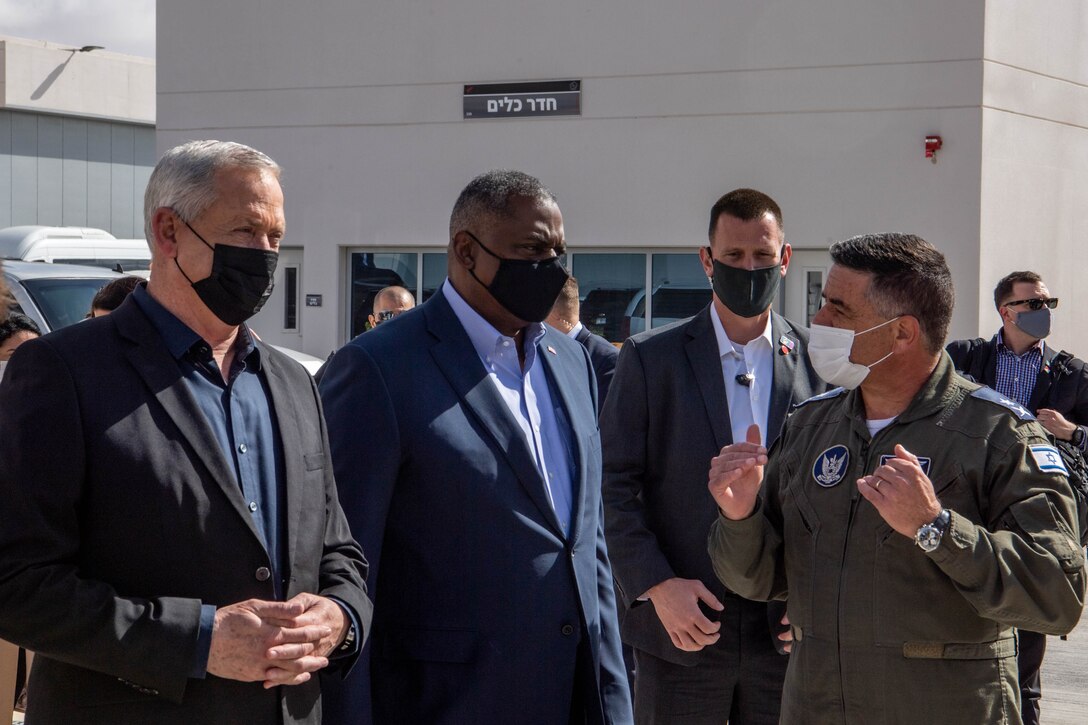 Secretary of Defense Lloyd J. Austin III and other officials listen to a service member speaking outside a building.