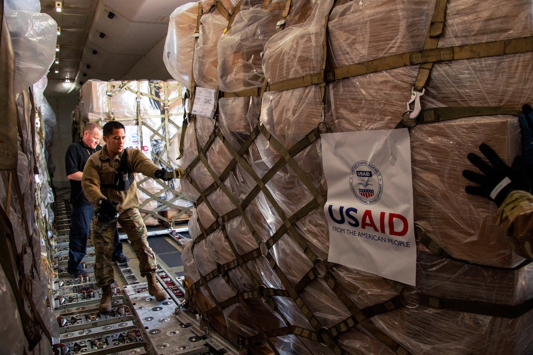 An airmen wearing gloves and another man load cargo into a plane.