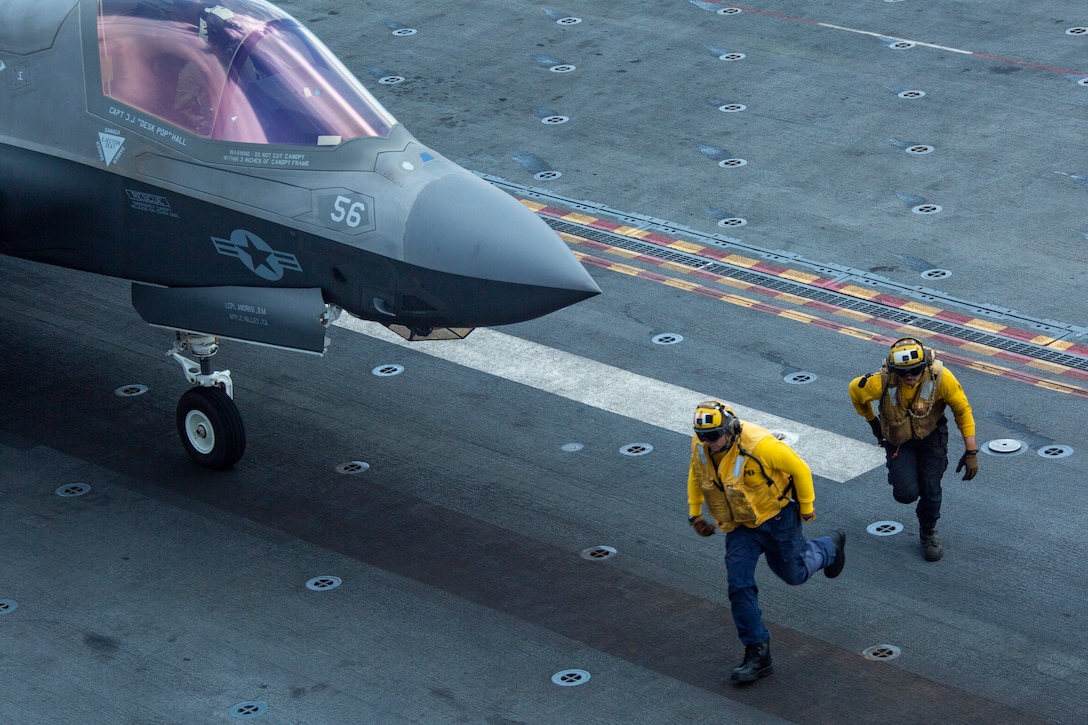 Sailors run in front of an F-35 aircraft readying for take off from the USS Makin Island.