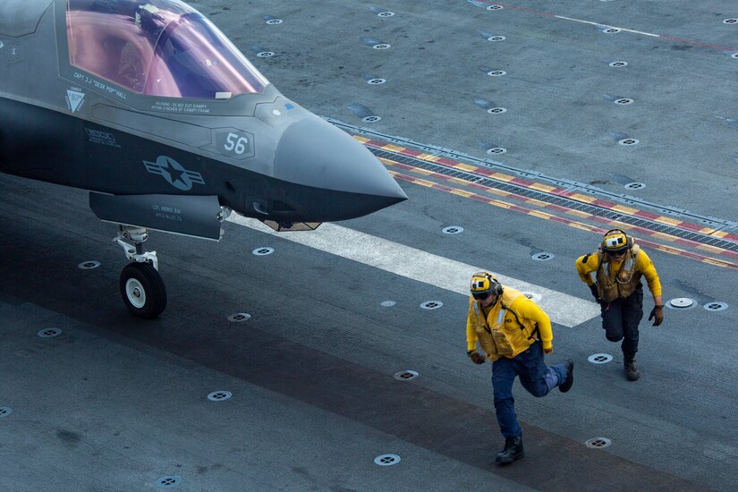 Sailors run in front of an F-35 aircraft readying for take off from the USS Makin Island.