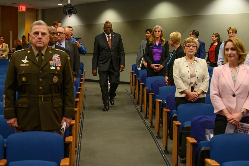 Secretary of Defense Lloyd J. Austin III walks down an aisle in an auditorium.