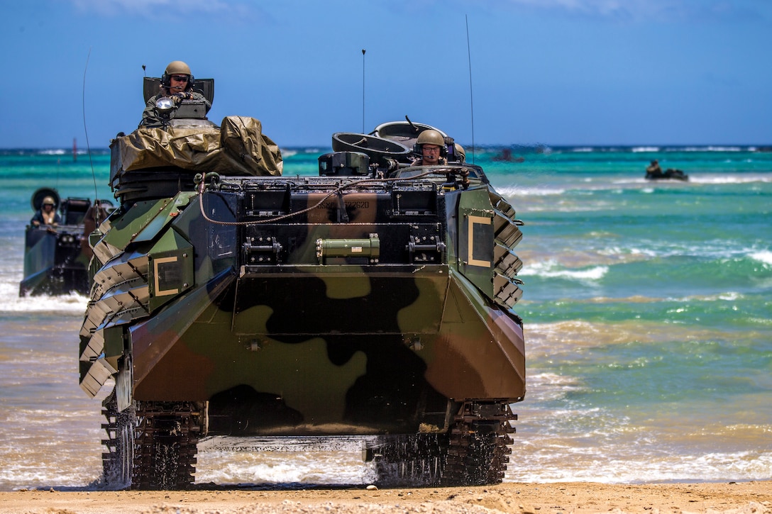 Marines travel in assault amphibious vehicles on a beach.