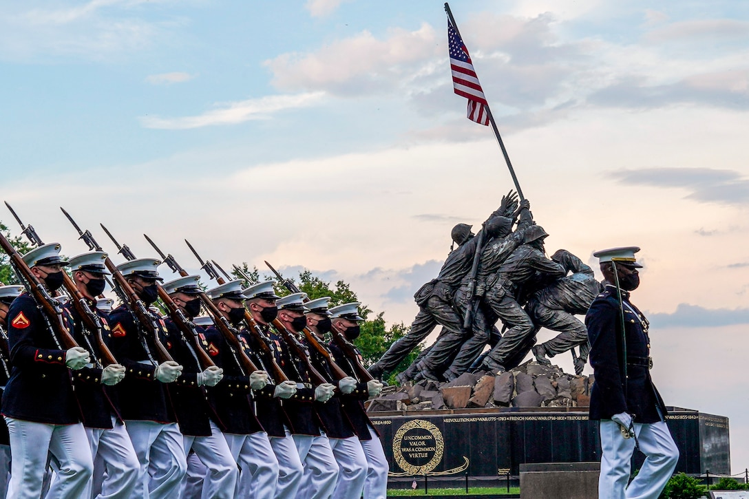 A statue showing Marines raising the American flag on Iwo Jima is framed by marching Marines.