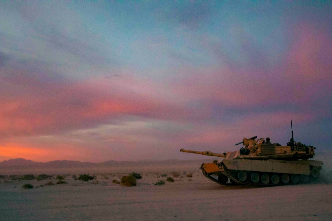 An Army tank drives through desert terrain.