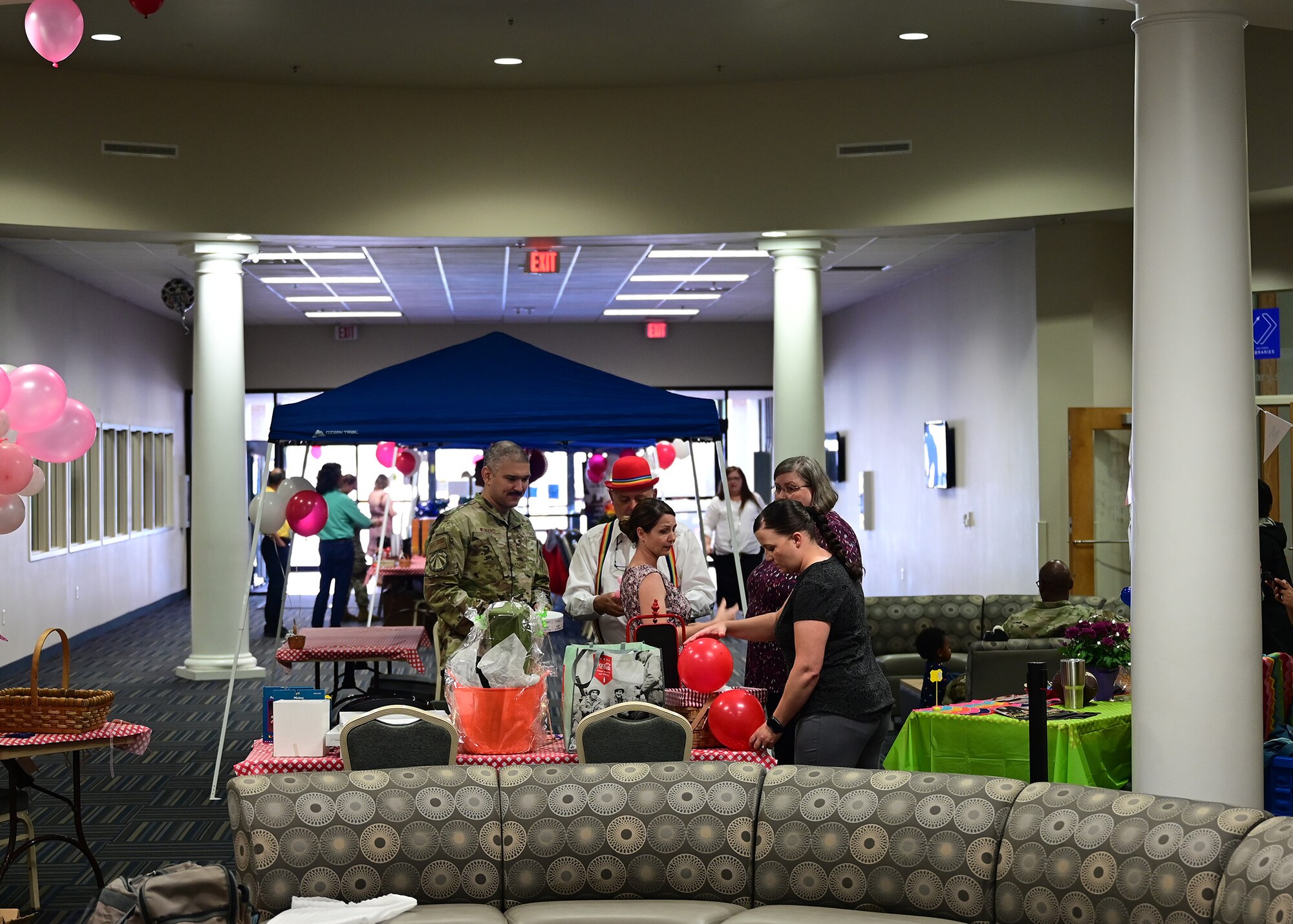 Airmen and their families stand around tents with tables under them.