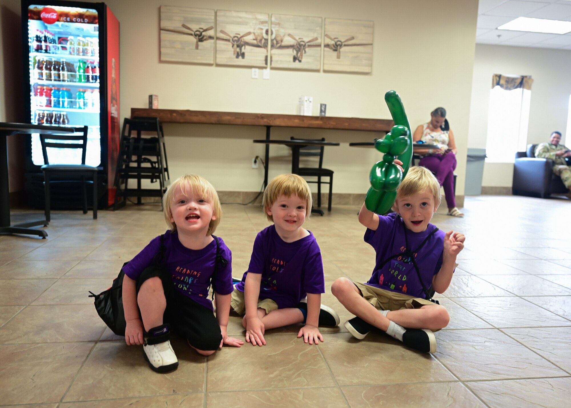 Three children sit on the floor while smiling.