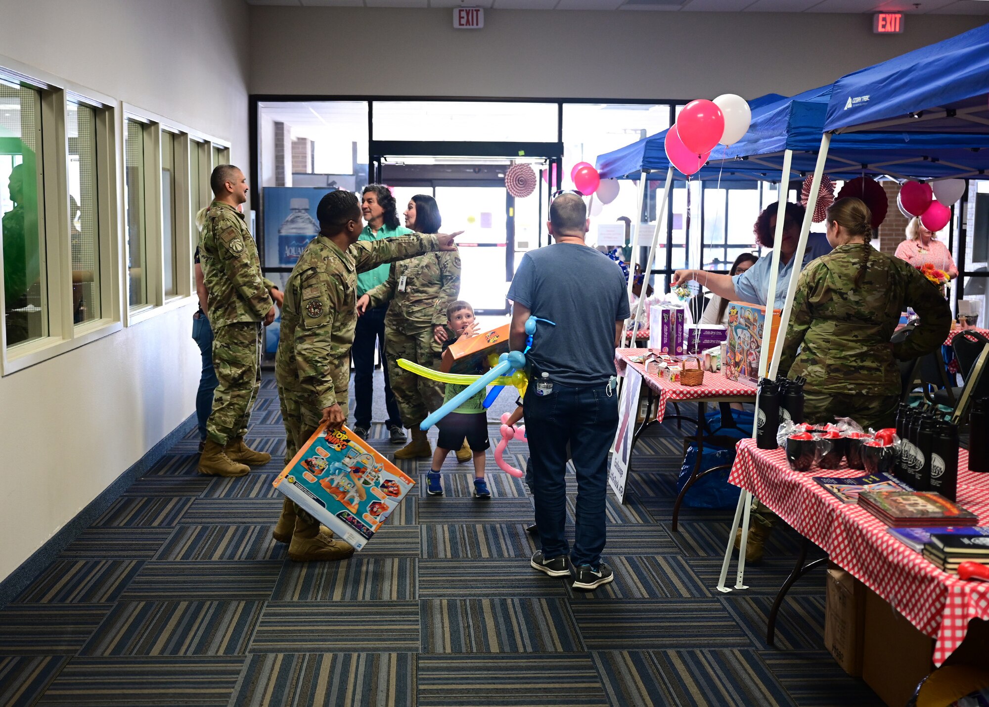 Airmen and families stand near blue tents with tables under them that contain gifts and information.
