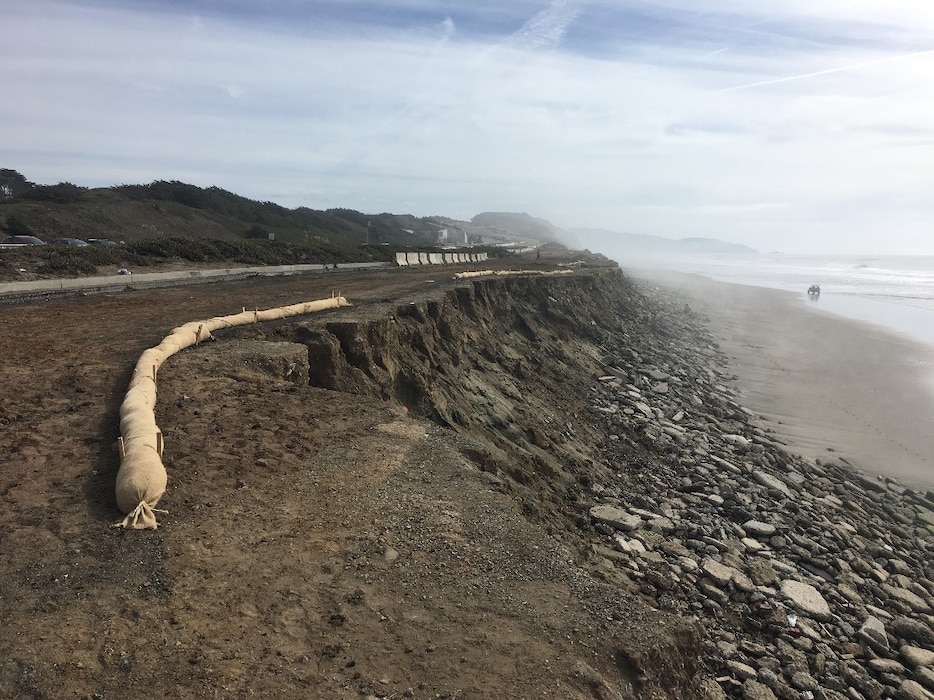 photo of brown sand dropping off drastically toward the water with rocks down below.