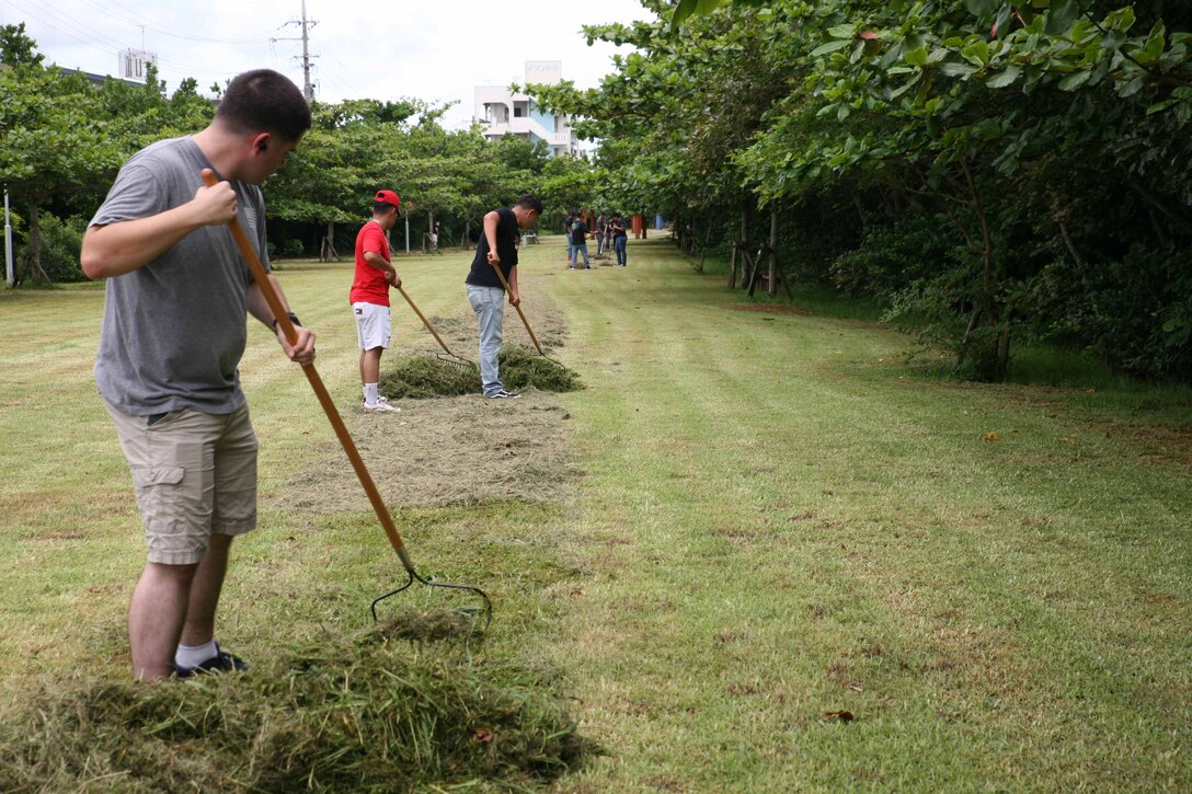伊芸海浜公園の駐車場の側にある芝生で、刈り取られた芝をレーキで集める海兵隊員の一団、沖縄県金武町、２０２１年６月９日