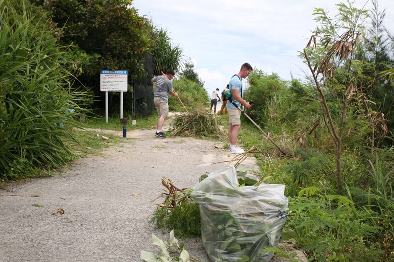 伊芸海浜公園の浜辺沿いにある歩道で、雑草を刈り集める海兵隊員、沖縄県金武町、２０２１年６月９日
