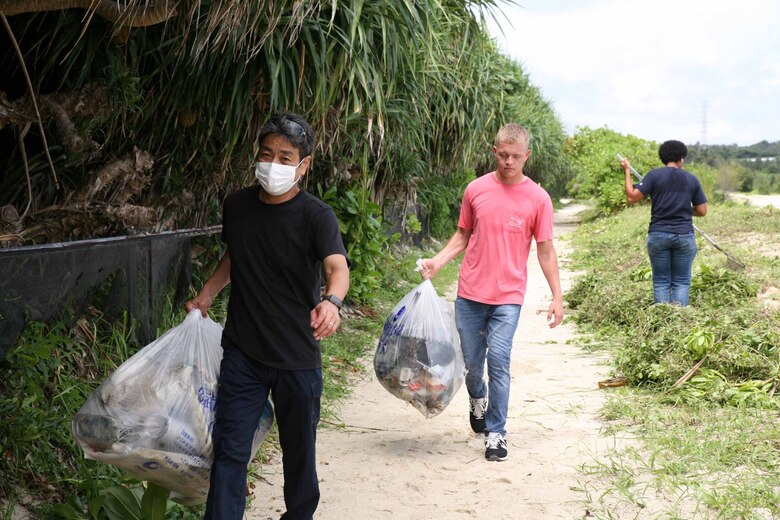 伊芸海浜公園の浜辺で集められたゴミを運ぶキャンプ・ハンセンの嘉陽基地渉外官と海兵隊員、沖縄県金武町、２０２１年６月９日