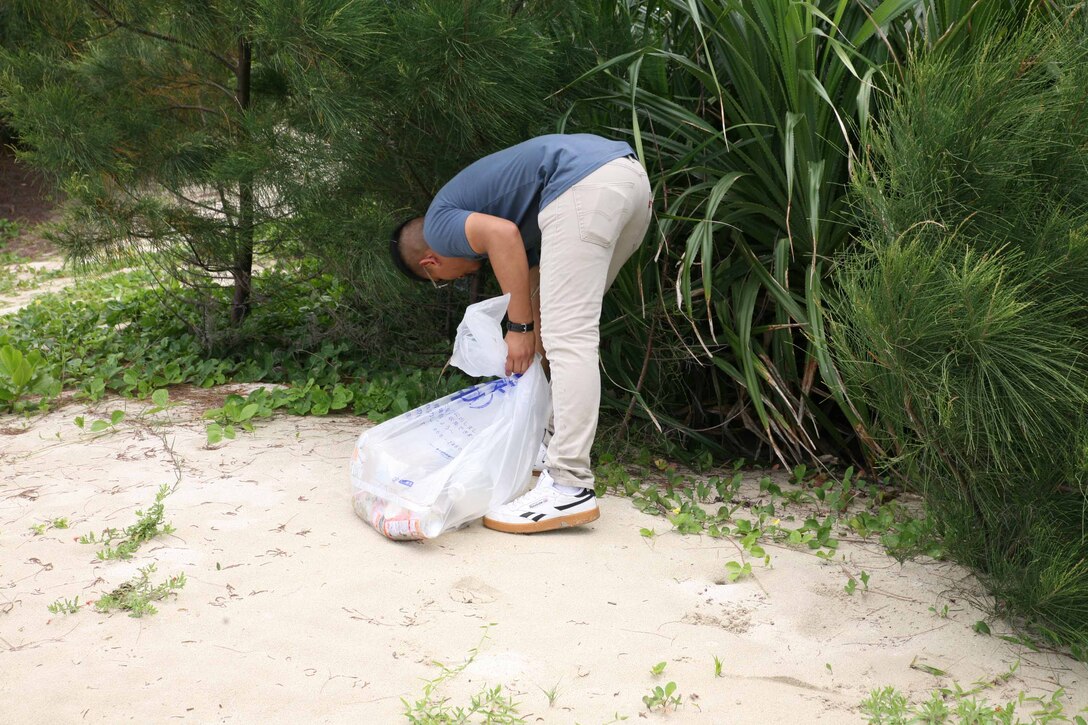 伊芸海浜公園の浜辺に生えている草木の中に捨てられているペットボトルや空き缶を拾い集める海兵隊員、沖縄県金武町、２０２１年６月９日