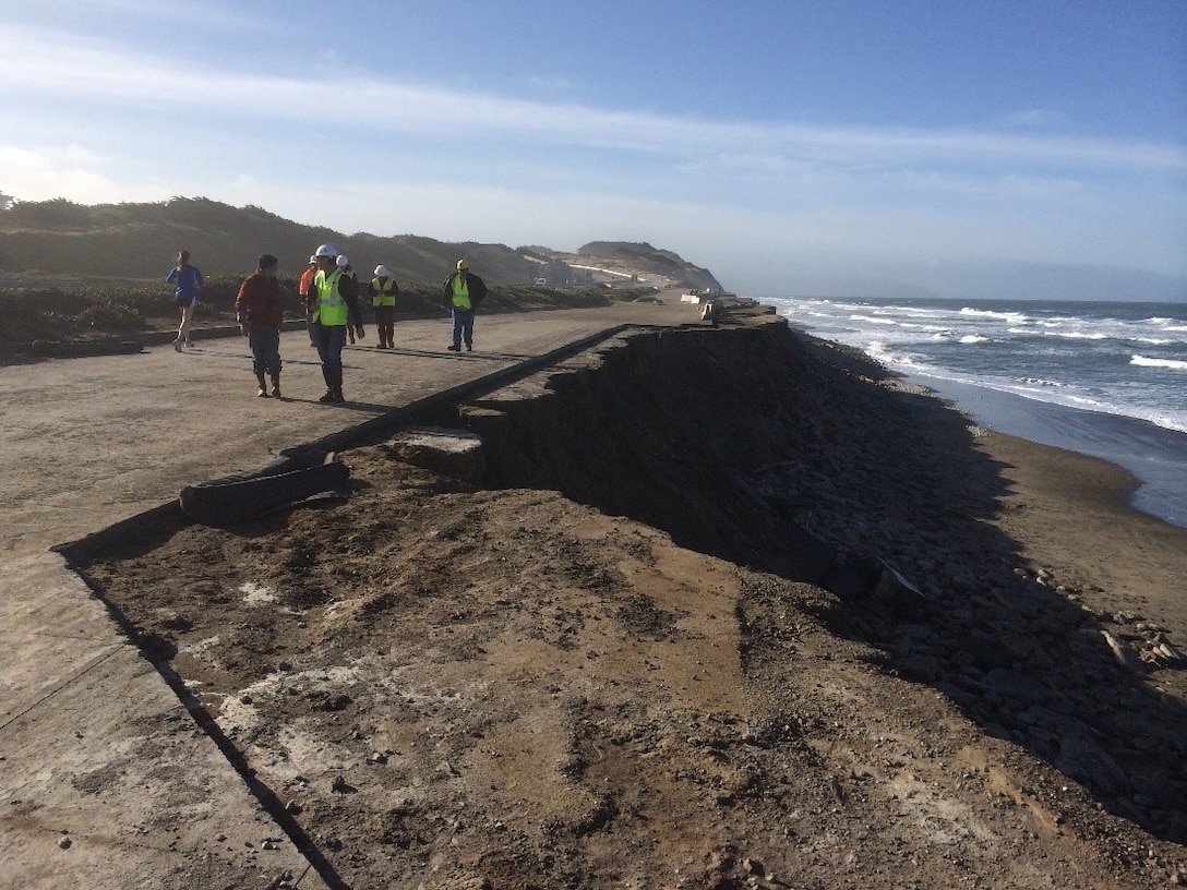 photo of sidewalk up on a bluff with a sharp drop off of eroded sand next to it.