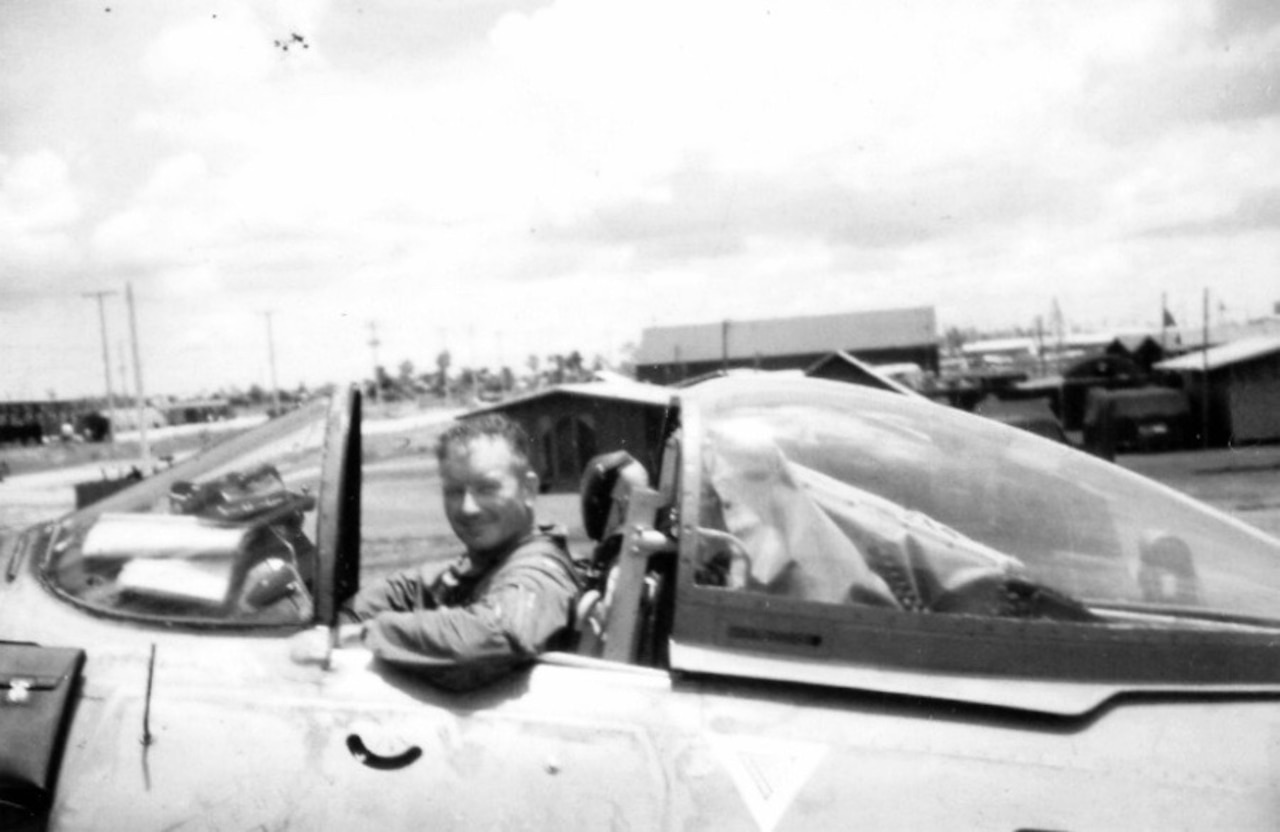 A pilot smiles from the open cockpit of a small, single-seat airplane.