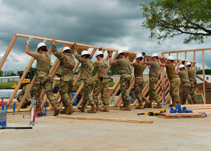 Airmen from all trades, with the 176th Wing’s Civil Engineer Squadron, raise the second exterior wall in unison as they construct the first home in the Cherokee Veterans Housing Initiative in Tahlequah, Oklahoma, May 18, 2021. The initiative is a collaboration between the Department of Defense’s Innovative Readiness Training program and the Cherokee Nation that constructs new single-family homes and supporting infrastructure for eligible Cherokee Nation veterans and their families. (U.S. Air Guard photo by Staff Sgt. Clay Cook)