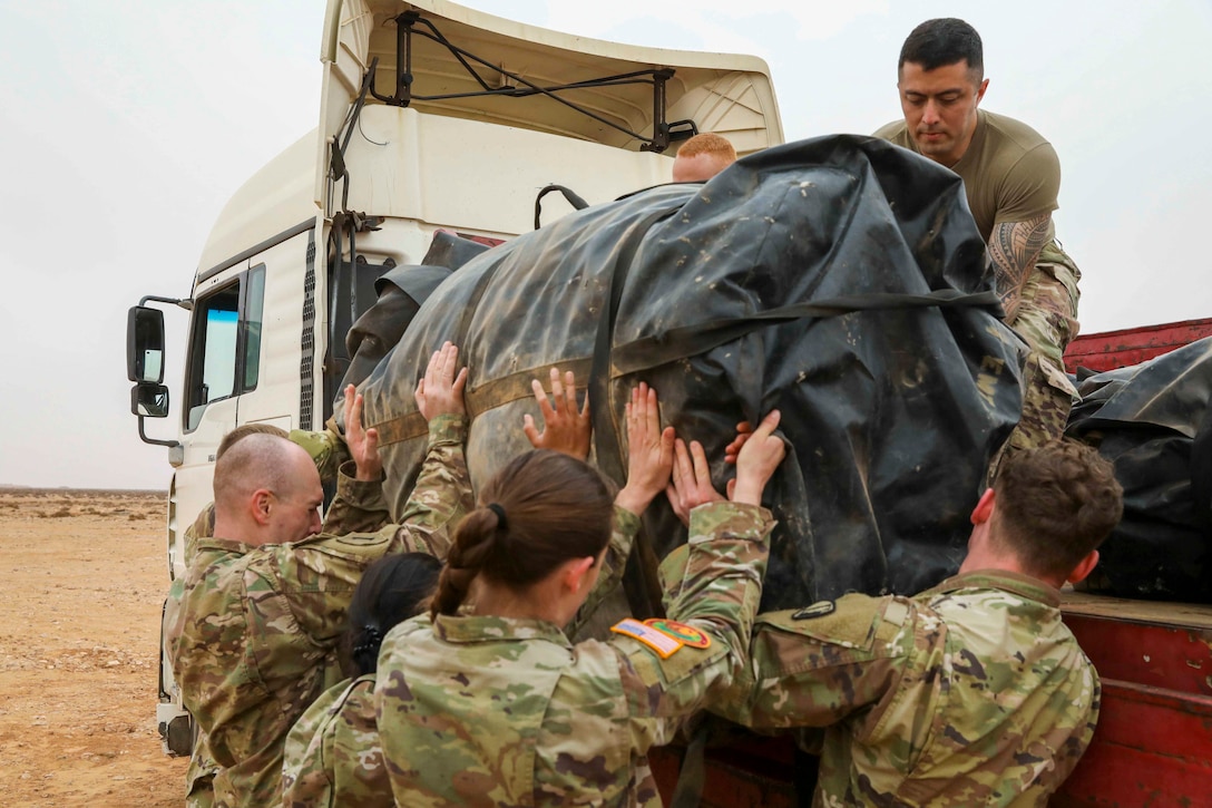 Guardsmen lift a large duffle bag into a vehicle.