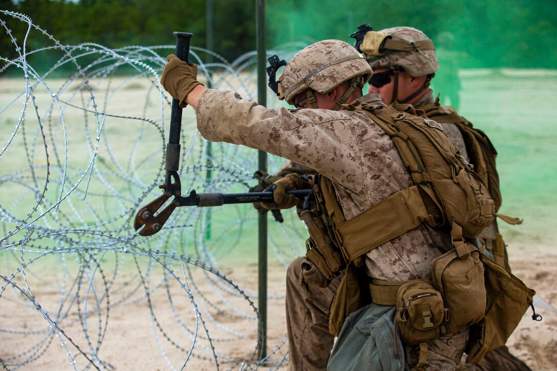 A Marine uses wire cutters to cut barbed wire as another Marine watches.