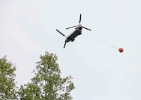 A 1st Battalion, 207th Aviation Regiment CH-47 Chinook helicopter with a Bambi water bucket system attached flies overhead during the unit's Red Card certification on Joint Base Elmendorf-Richardson, June 9, 2021. Red Card certification, also known as the Incident Qualification Card, is an accepted interagency certification that a person is qualified in order to accomplish the required mission when arriving on an incident. For 1-207th AVN pilots, this certification means proficiency in water bucket drops to assist with wildfire emergencies within the state. (U.S. Army National Guard photo by Spc. Grace Nechanicky)