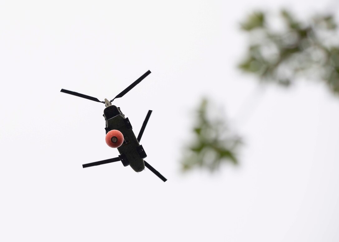 A 1st Battalion, 207th Aviation Regiment CH-47 Chinook helicopter with a Bambi water bucket system attached flies overhead during the unit's Red Card certification on Joint Base Elmendorf-Richardson, June 9, 2021. Red Card certification, also known as the Incident Qualification Card, is an accepted interagency certification that a person is qualified in order to accomplish the required mission when arriving on an incident. For 1-207th AVN pilots, this certification means proficiency in water bucket drops to assist with wildfire emergencies within the state. (U.S. Army National Guard photo by Spc. Grace Nechanicky)