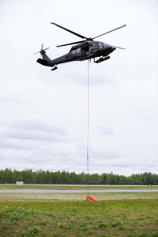 Pilots and crew members of the 207th Aviation Battalion attach a Bambi water bucket system to a UH-60 Black Hawk helicopter to complete their Red Card certification on Joint Base Elmendorf-Richardson, June 9, 2021. Red Card certification, also known as the Incident Qualification Card, is an accepted interagency certification that a person is qualified in order to accomplish the required mission when arriving on an incident. For 1-207th AVN pilots, this certification means proficiency in water bucket drops to assist with wildfire emergencies within the state. (U.S. Army National Guard photo by Spc. Grace Nechanicky)
