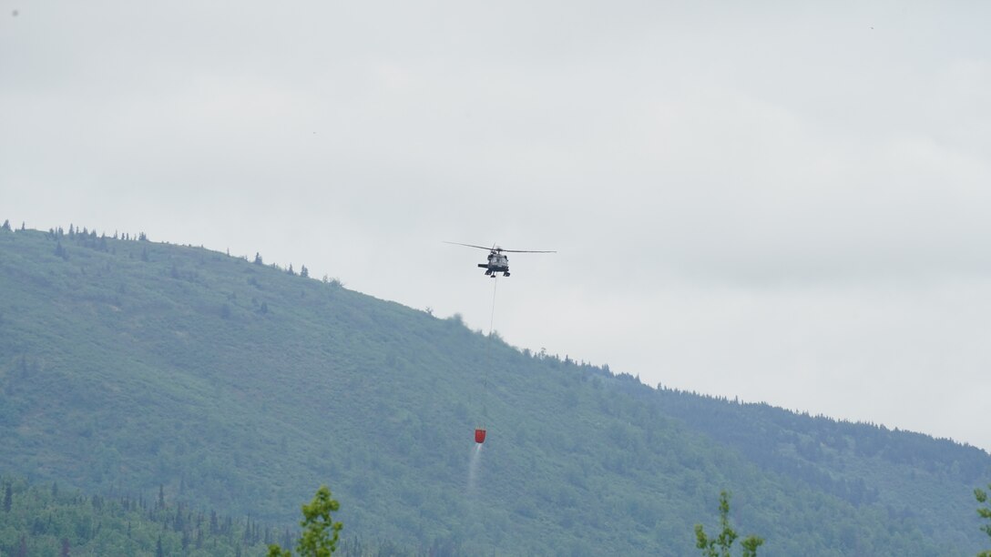 A 1st Battalion, 207th Aviation Regiment UH-60 Black Hawk helicopter with a Bambi water bucket system attached flies overhead during the unit's Red Card certification on Joint Base Elmendorf-Richardson, June 9, 2021. Red Card certification, also known as the Incident Qualification Card, is an accepted interagency certification that a person is qualified in order to accomplish the required mission when arriving on an incident. For 1-207th AVN pilots, this certification means proficiency in water bucket drops to assist with wildfire emergencies within the state. (U.S. Army National Guard photo by Dana Rosso)
