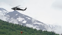 A 1st Battalion, 207th Aviation Regiment UH-60 Black Hawk helicopter with a Bambi water bucket system attached flies overhead during the unit's Red Card certification on Joint Base Elmendorf-Richardson, June 9, 2021. Red Card certification, also known as the Incident Qualification Card, is an accepted interagency certification that a person is qualified in order to accomplish the required mission when arriving on an incident. For 1-207th AVN pilots, this certification means proficiency in water bucket drops to assist with wildfire emergencies within the state. (U.S. Army National Guard photo by Dana Rosso)