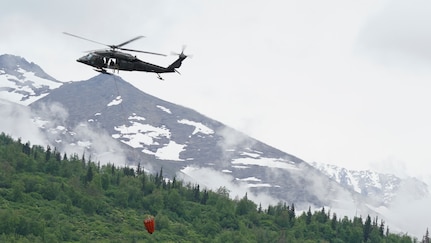 A 1st Battalion, 207th Aviation Regiment UH-60 Black Hawk helicopter with a Bambi water bucket system attached flies overhead during the unit's Red Card certification on Joint Base Elmendorf-Richardson, June 9, 2021. Red Card certification, also known as the Incident Qualification Card, is an accepted interagency certification that a person is qualified in order to accomplish the required mission when arriving on an incident. For 1-207th AVN pilots, this certification means proficiency in water bucket drops to assist with wildfire emergencies within the state. (U.S. Army National Guard photo by Dana Rosso)