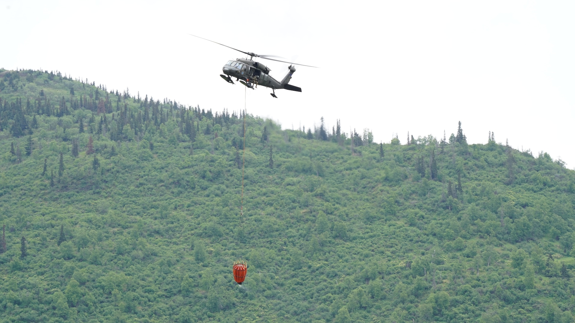 A 1st Battalion, 207th Aviation Regiment UH-60 Black Hawk helicopter with a Bambi water bucket system attached flies overhead during the unit's Red Card certification on Joint Base Elmendorf-Richardson, June 9, 2021. Red Card certification, also known as the Incident Qualification Card, is an accepted interagency certification that a person is qualified in order to accomplish the required mission when arriving on an incident. For 1-207th AVN pilots, this certification means proficiency in water bucket drops to assist with wildfire emergencies within the state. (U.S. Army National Guard photo by Dana Rosso)