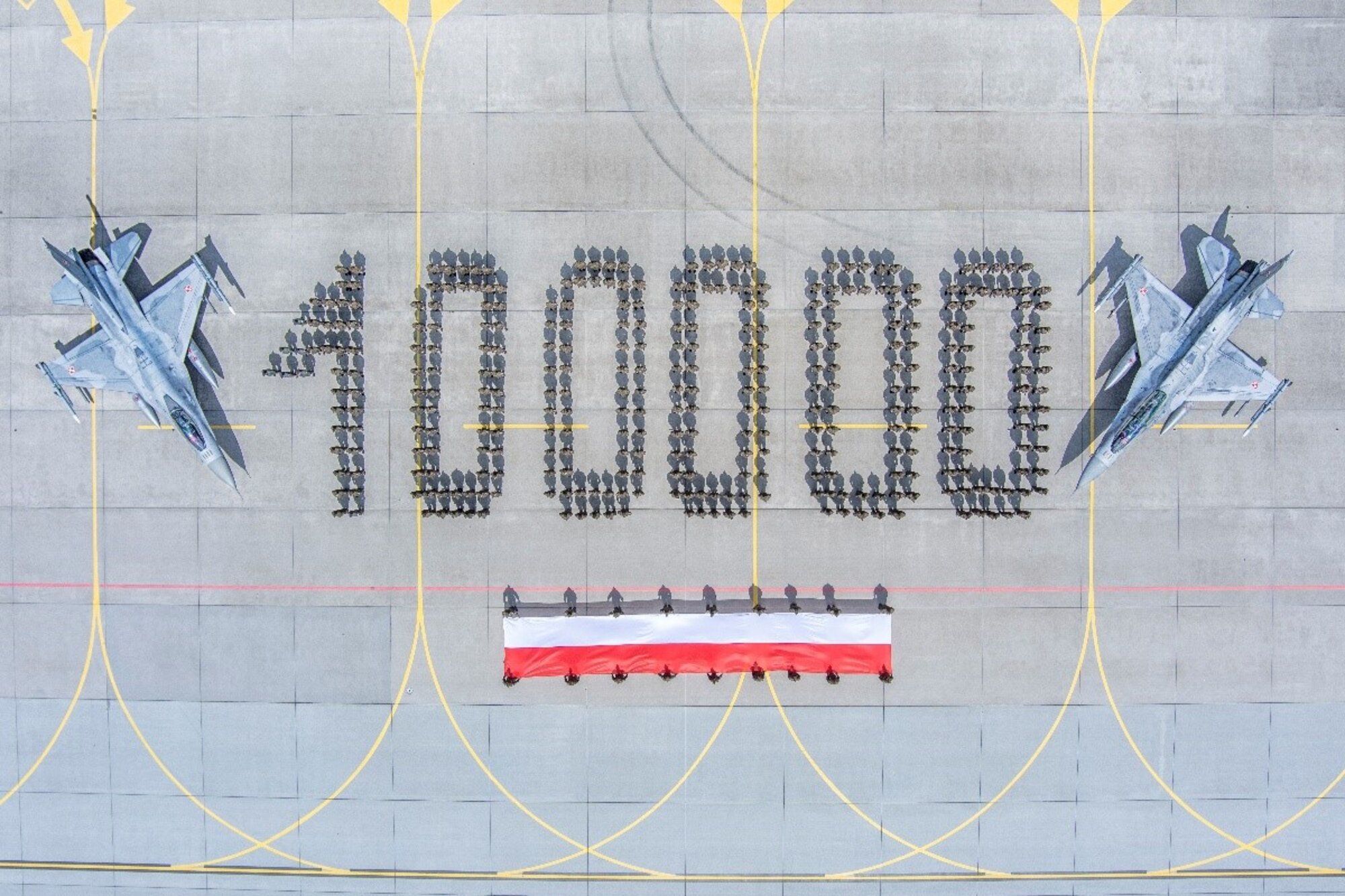 The Polish Air Force celebrates 100,000 flight hours of its F-16 aircraft fleet, by staging a photo with its airmen standing in formation to form “100000” when read from the sky. The airmen in the photo are accompanied by the Polish flag and two of the aircraft acquired from the United States. (Courtesy photo)