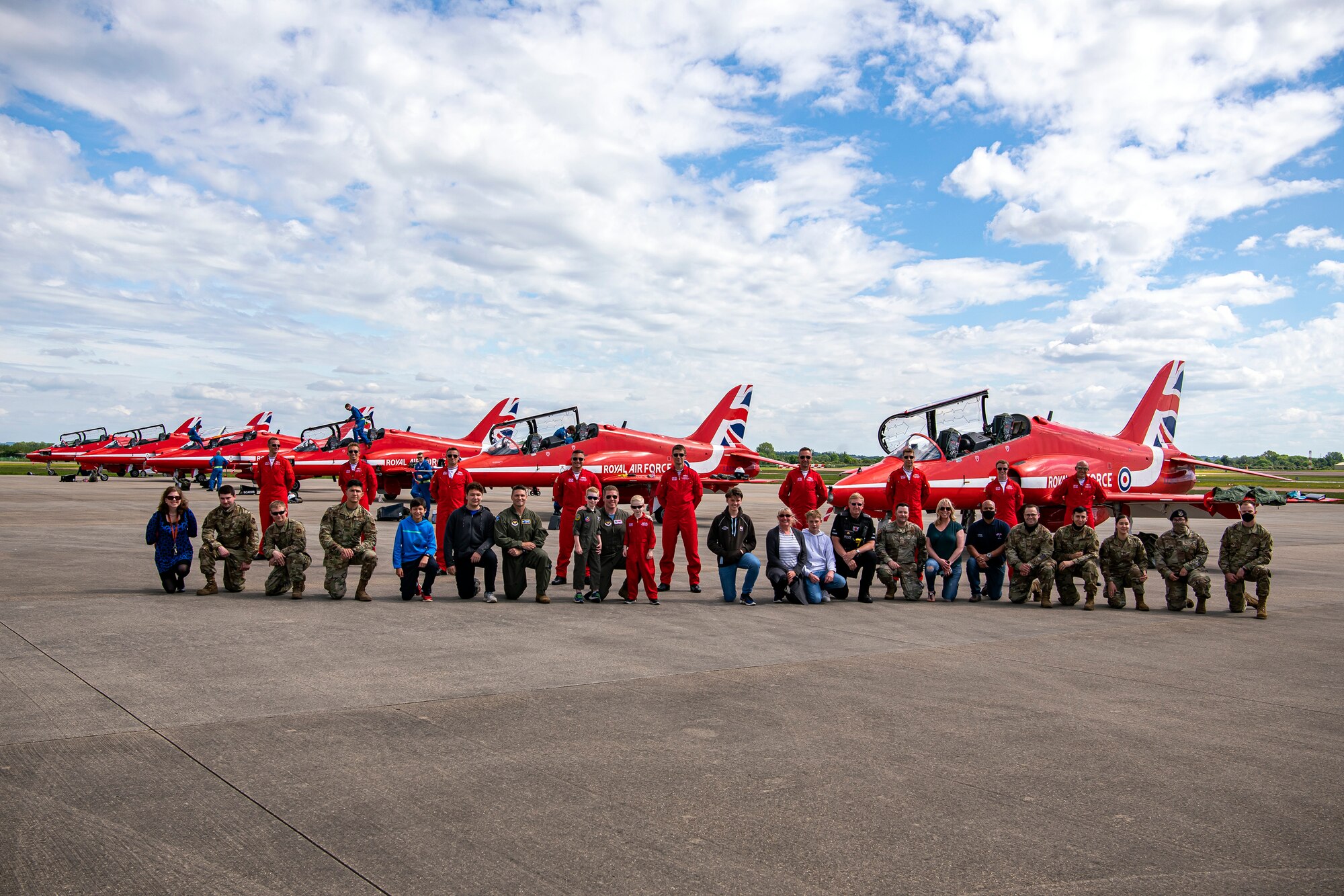 Airmen and spectators from the 501st Combat Support Wing, pose for a photo along with the pilots from Royal Air Force aerobatic team, known as the Red Arrows at RAF Fairford, England, June 4, 2021. The Red Arrows landed at Fairford to refuel in preparation for the Midlands Air Festival. The pilots and crew members were able to integrate and meet with Airmen from the 501st Combat Support Wing. (U.S. Air Force photo by Senior Airman Eugene Oliver