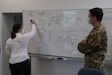 Joint Security Coordination Center Chief of Protection Patricia Giera, 7th Mission Support Command, explains the JSCC structure to Hungarian military police officer Capt. Zoltan Szentpeteri on Panzer Kaserne in Kaiserslautern, Germany, May 27, 2021. U.S. Army Reserve Soldiers and Civilians assigned to the 7th MSC teamed up with NATO Allies and partners from 18 different countries to provide a unique protection capability for U.S. Army Europe and Africa by serving as the JSCC in support of DEFENDER Europe 21. (U.S. Army Reserve Photo by Capt. Lorenzo Llorente)