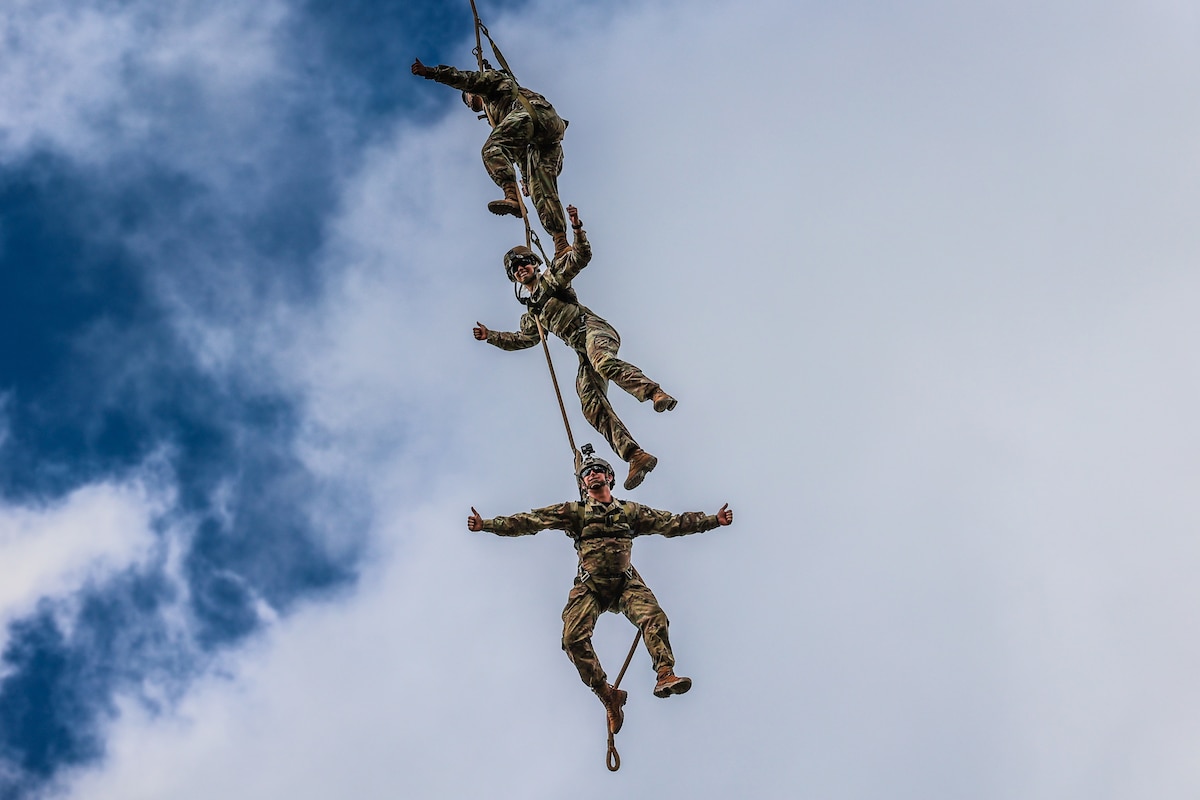 Three soldiers hang above each other on a rope in midair.