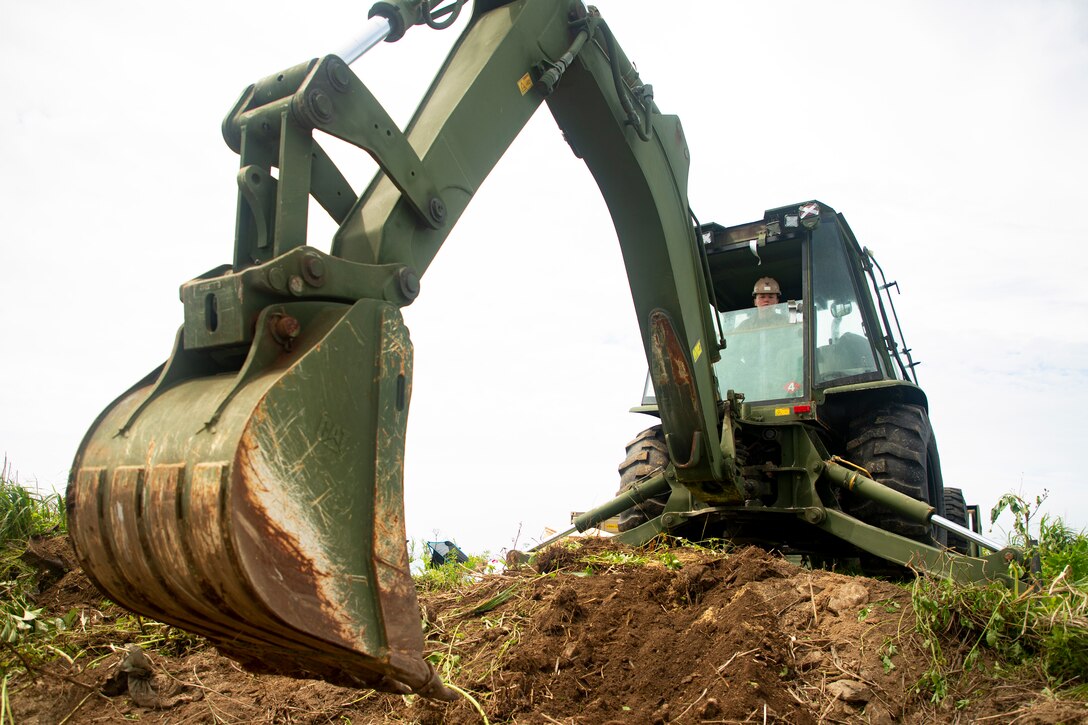 A sailor digs a large trench using a backhoe.