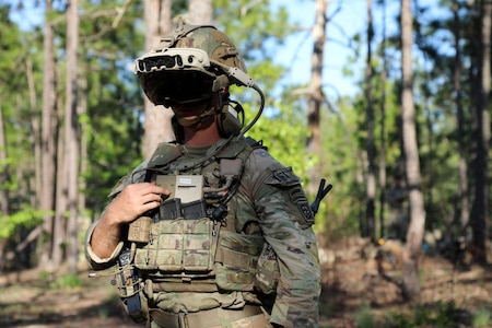 Photo of a soldier in a wooded area, wearing a mixed-reality headset during a training exercise.