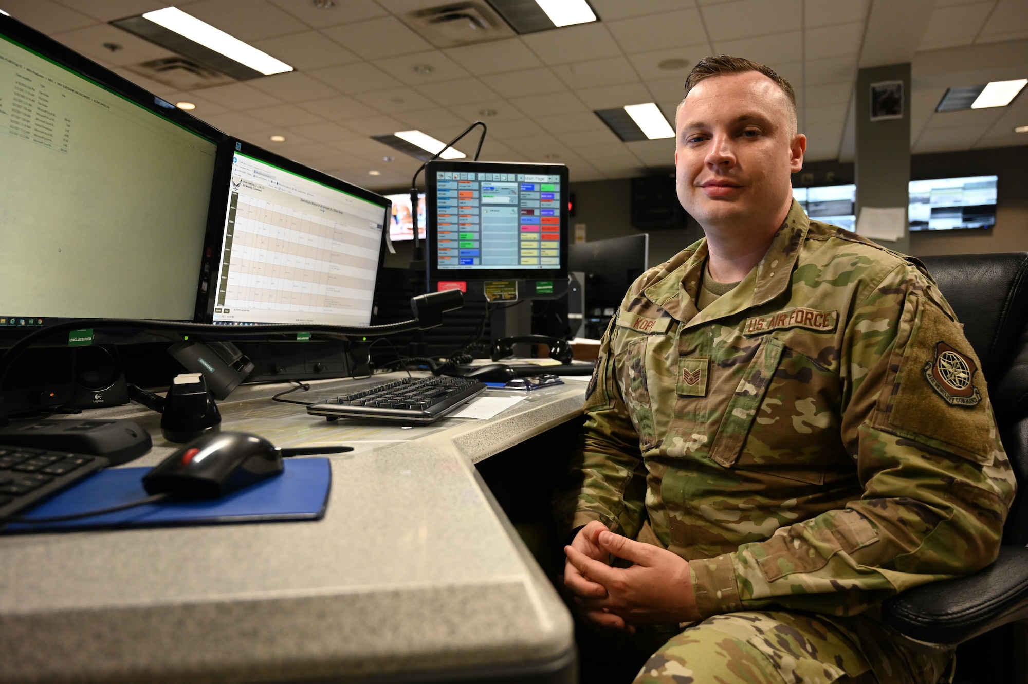 An airman poses for a photo at a desk.
