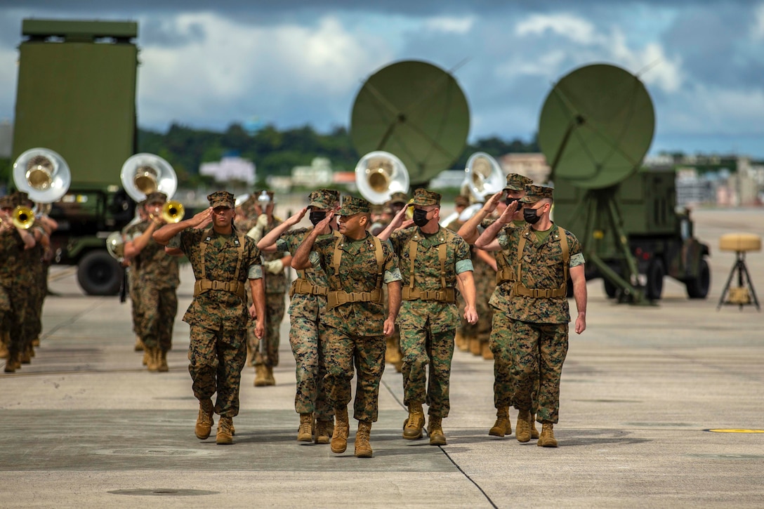 Marines salute while marching in formation.