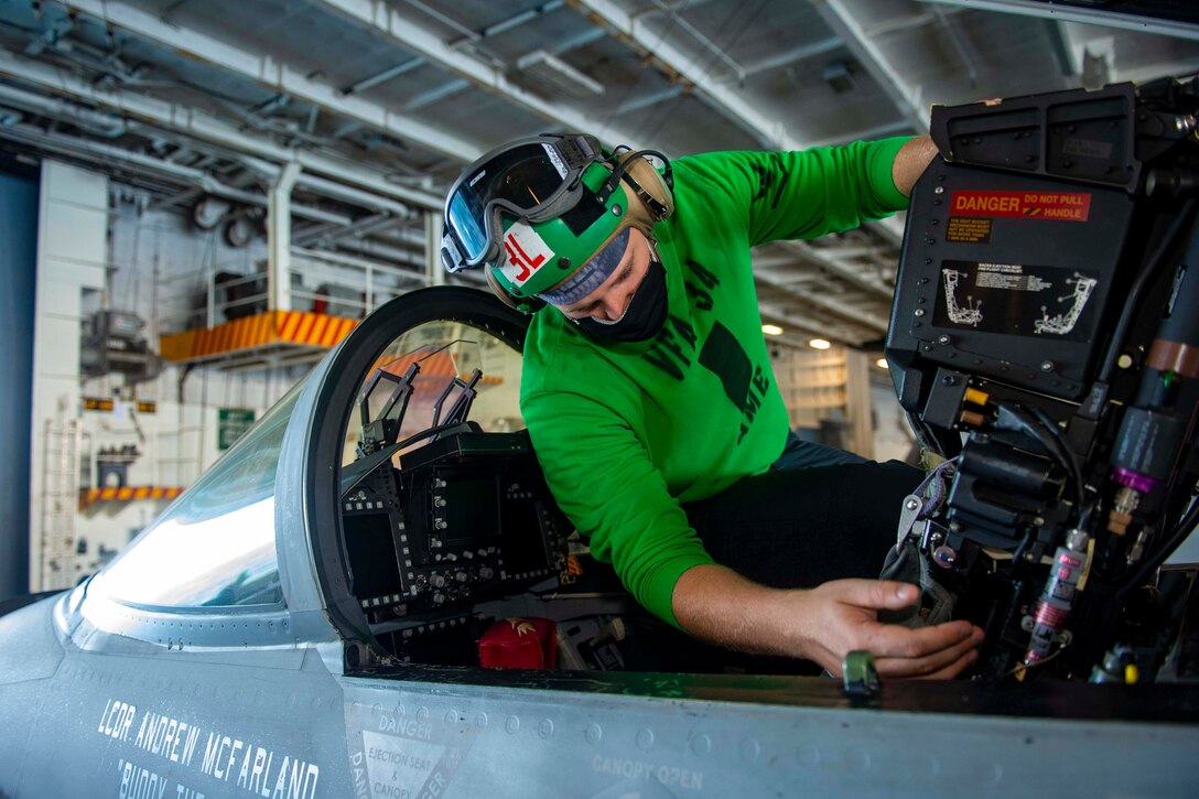 A sailor inspects the cockpit of a jet.