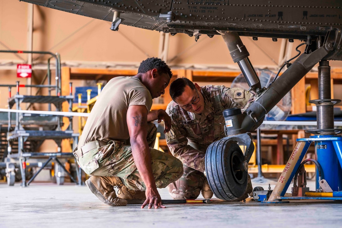 Two soldiers replace a tire on a helicopter.