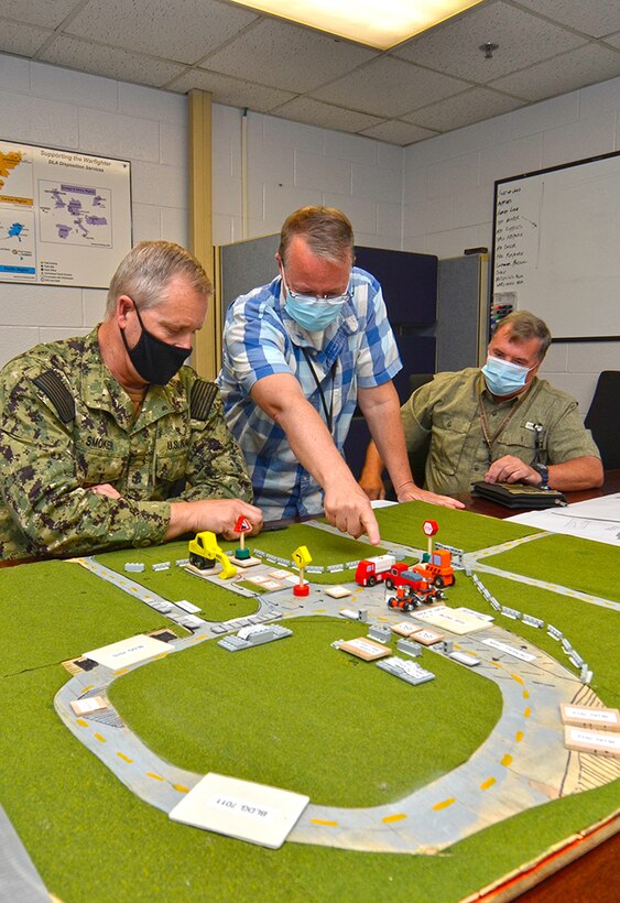 Three men look at a model practice site do determine where things should be placed.